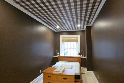 Cozy bedroom featuring dark brown walls, a checkered ceiling, a wooden bed with white bedding, and a window with blinds, showcasing Wilder Painting's residential design style.